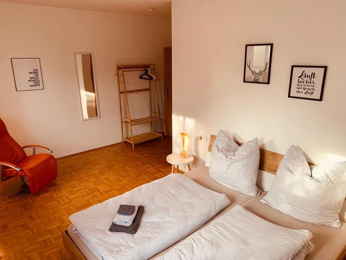 Ein Zimmer mit einem Bett, einem roten Sessel, einem kleinen Tisch mit einer Lampe und einer an der Wand stehenden Leiter.