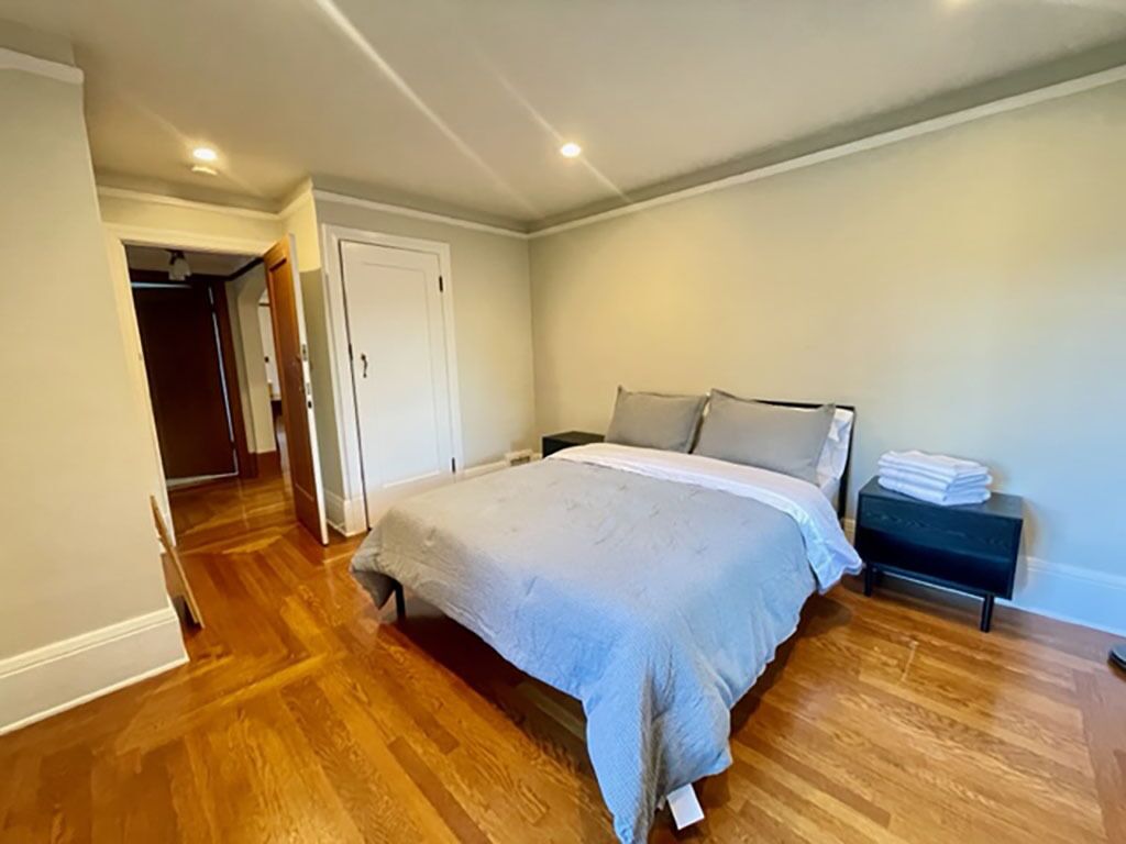 A bedroom with a large bed, wooden flooring, a bedside table, and a nightstand.