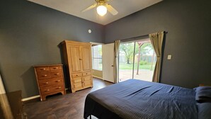 A bedroom with a bed, a wooden dresser, and a sliding glass door leading to a patio.