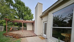 A backyard with a wooden deck, a pergola, a chimney, and a large window.