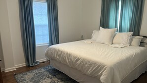 Una cama bien hecha con sábanas blancas, una alfombra estampada y cortinas azules.