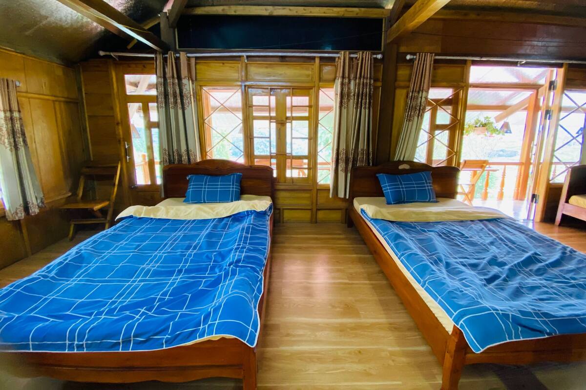 A room with two wooden beds, each with a blue bedspread and matching pillows. The room has wooden walls and a wooden ceiling.