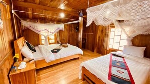 A wooden cabin bedroom with two beds, a wooden nightstand, and a hanging light fixture. - Peace Home (Ta Van)