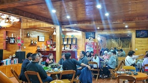 A wooden interior with tables and chairs, a bar area, and a television screen. - Peace Home (Ta Van)