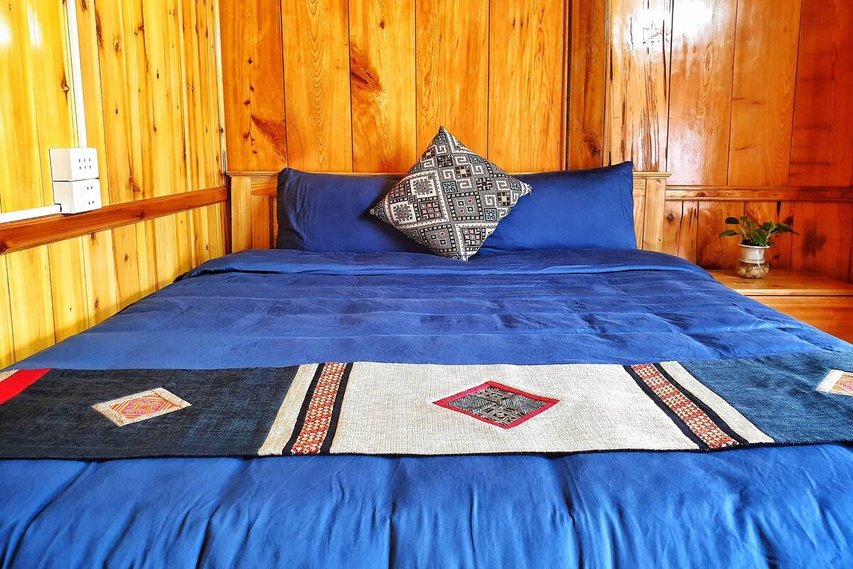 A wooden-paneled room with a bed featuring a blue bedspread and a patterned pillow.