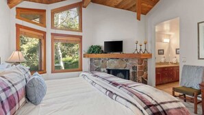 A bedroom with a bed, a television, a stone fireplace, and large windows. - Abode at Crescent Cabin, private hot tub, pool, mountain cabin (Park City)