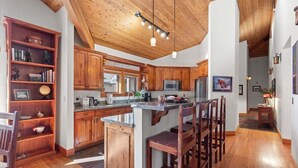 A spacious kitchen with wooden cabinets, a central island with bar stools, and pendant lighting. - Abode at Crescent Cabin, private hot tub, pool, mountain cabin (Park City)