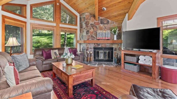 A spacious living room with a stone fireplace, a large TV, and a cozy seating area. - Abode at Crescent Cabin, private hot tub, pool, mountain cabin (Park City)
