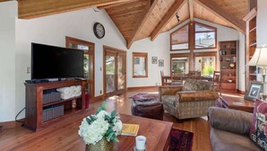 A spacious living room with a wooden ceiling, a flat-screen TV on a wooden stand, a sofa, a coffee table, and a bookshelf. - Abode at Crescent Cabin, private hot tub, pool, mountain cabin (Park City)