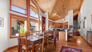 A spacious kitchen with wooden cabinets, a dining area with a large table and chairs, and a view of the outdoors through large windows. - Abode at Crescent Cabin, private hot tub, pool, mountain cabin (Park City)