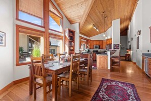 Una cocina amplia con armarios de madera, un comedor con una mesa grande y sillas, y vistas al exterior a través de ventanas grandes.