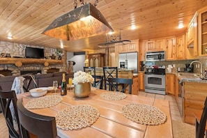 A wooden interior with a dining table, chairs, a kitchen area, and a fireplace.