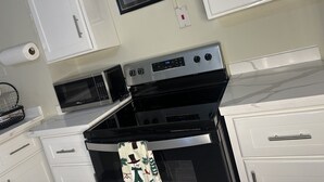 Een keuken met witte kastjes, een roestvrijstalen oven, een magnetron en een ingelijst schilderij aan de muur.