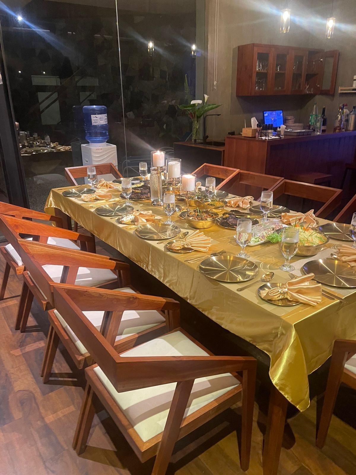 A dining area with a long table set for a meal, wooden chairs, and a view of the outside.