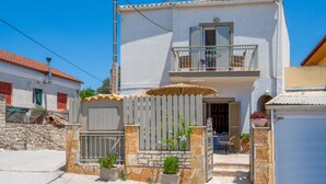 A two-story house with a balcony, a gated entrance with potted plants, and a clear blue sky.