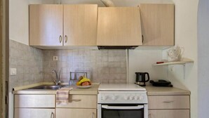 A compact kitchen with light wooden cabinets, a white tiled backsplash, a sink, a stove, and a kettle on the countertop.