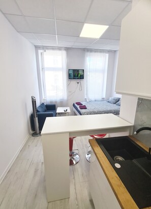 Een compacte hotelkamer met kitchenette, een bed, een klein zithoekje en een aan de muur bevestigde televisie.