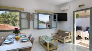 Un coin repas avec une table dressée pour quatre personnes, un canapé, un téléviseur fixé au mur et une porte ouverte donnant sur l’extérieur.