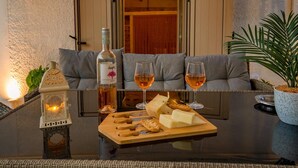 Un rincón acogedor con un espacio para sentarse y una mesa dispuesta para una comida, con queso, galletas y una botella de vino.