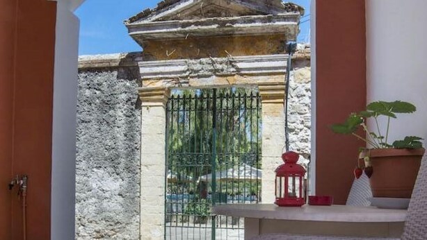 A balcony with a stone floor, a wicker chair, a table with a red lantern, and a potted plant. - Dora II Studio - Simple Sweet Getaway (Paxos)