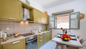 A compact kitchen with yellow cabinets, a built-in oven, and a dining area with a table set for two. - Dora II Studio - Simple Sweet Getaway (Paxos)