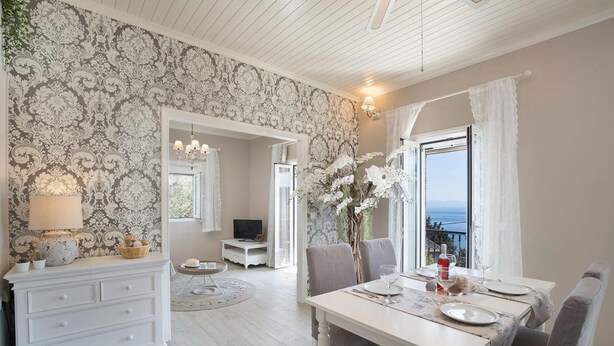 Ein Zimmer mit Esstisch für zwei Personen, einem weißen Kommode, einem Fernseher und Meerblick durch ein Fenster.