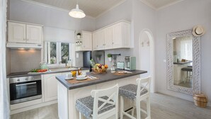 Eine Küche mit weißen Schränken, einer zentralen Kochinsel mit Stühlen, einem Vintage-Toaster und einem großen Spiegel mit ornamentalem Rahmen.