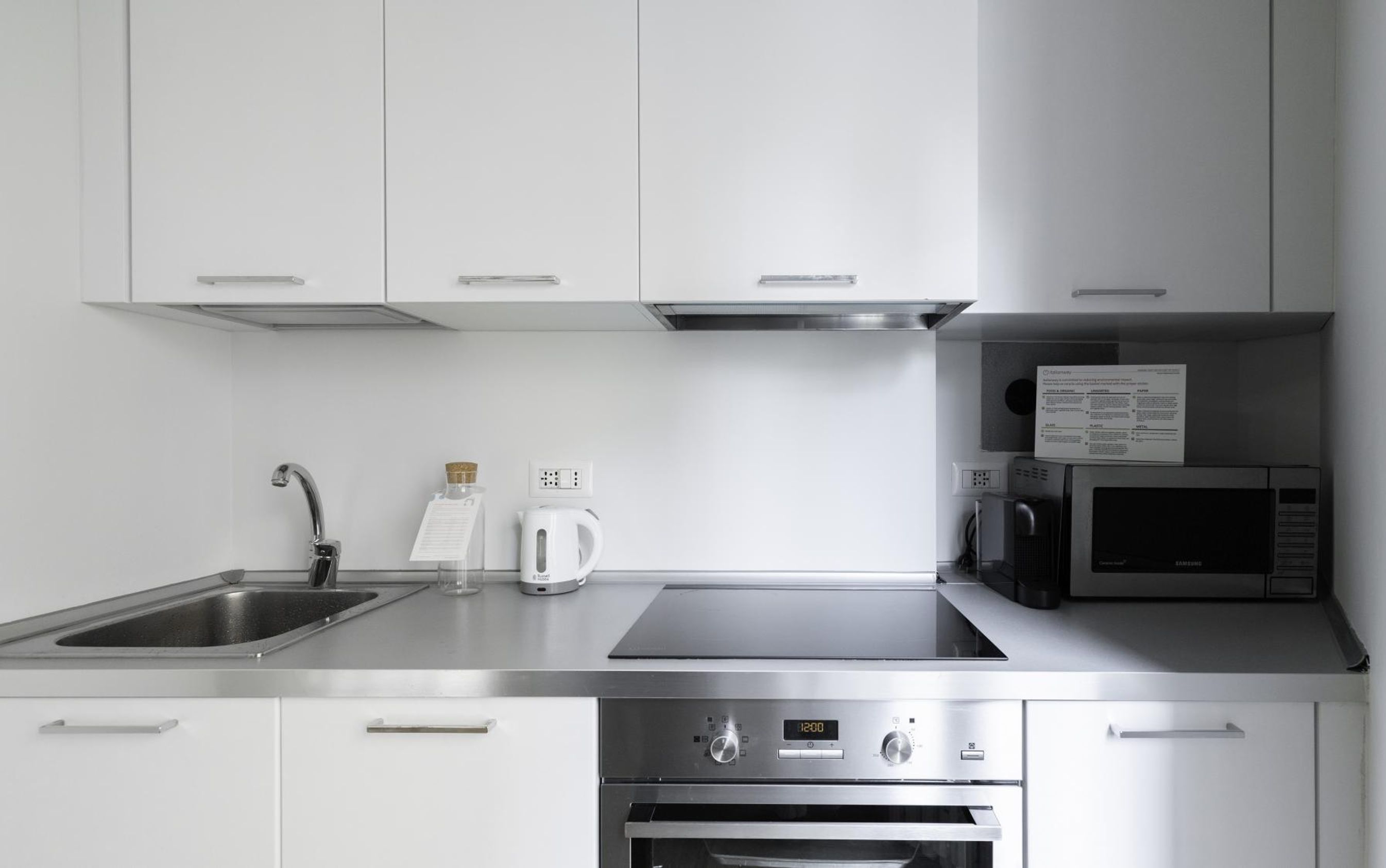 A modern kitchen with stainless steel appliances, including a microwave, oven, and kettle.