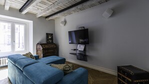 Un salon avec un canapé bleu, un téléviseur fixé au mur, un meuble en bois et une valise.