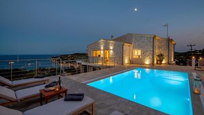 A stone villa with a swimming pool, outdoor seating, and a view of the sea.