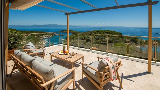 A balcony with a table, chairs, and a view of the sea and mountains.