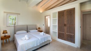 A bedroom with two beds, a wooden wardrobe, and a window with a view of greenery.