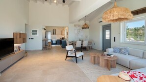 A spacious living area with a sofa, coffee table, and TV. There is a kitchen in the background with a dining area.