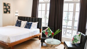A hotel room with a large bed, a small round table, a chair, and a view of the city through large windows. - Mettavary Hotel (Phnom Penh)