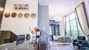 A hotel lobby with a reception desk, a chandelier, a sofa, and a large window offering a view of the outdoors. - Mettavary Hotel (Phnom Penh)