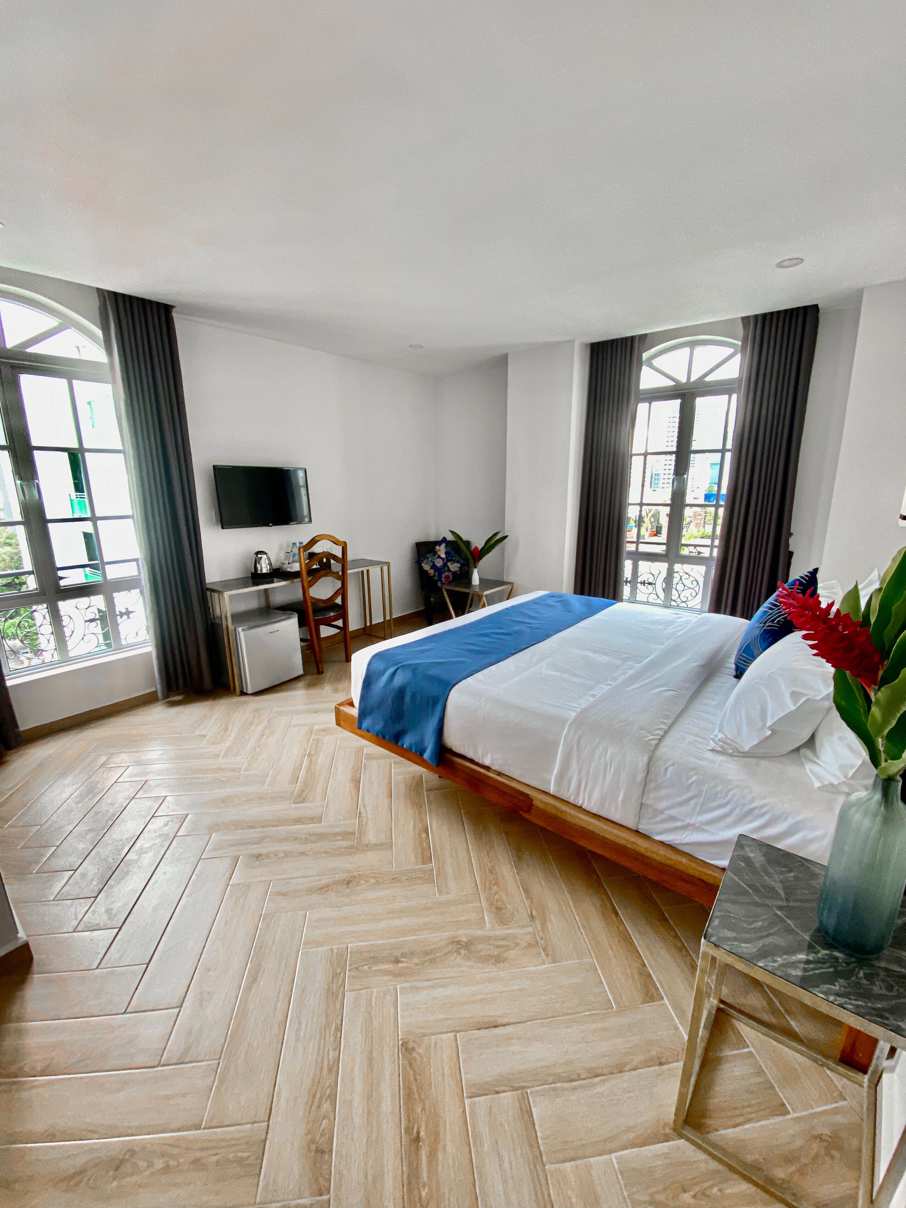 A hotel room with a bed, a desk, a chair, a TV, and a window with curtains.