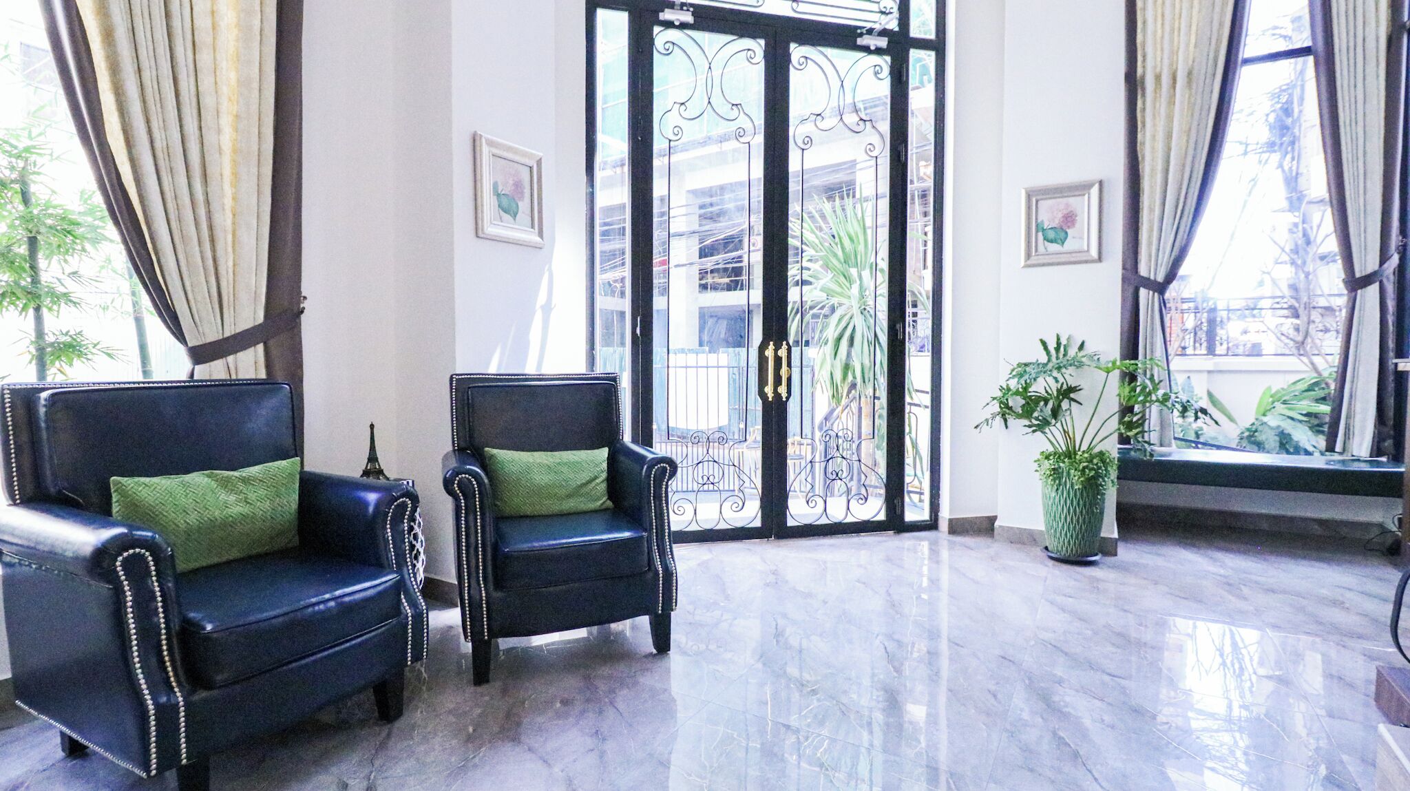 A lobby with two black leather armchairs with green cushions, a potted plant, and a glass door with decorative ironwork.