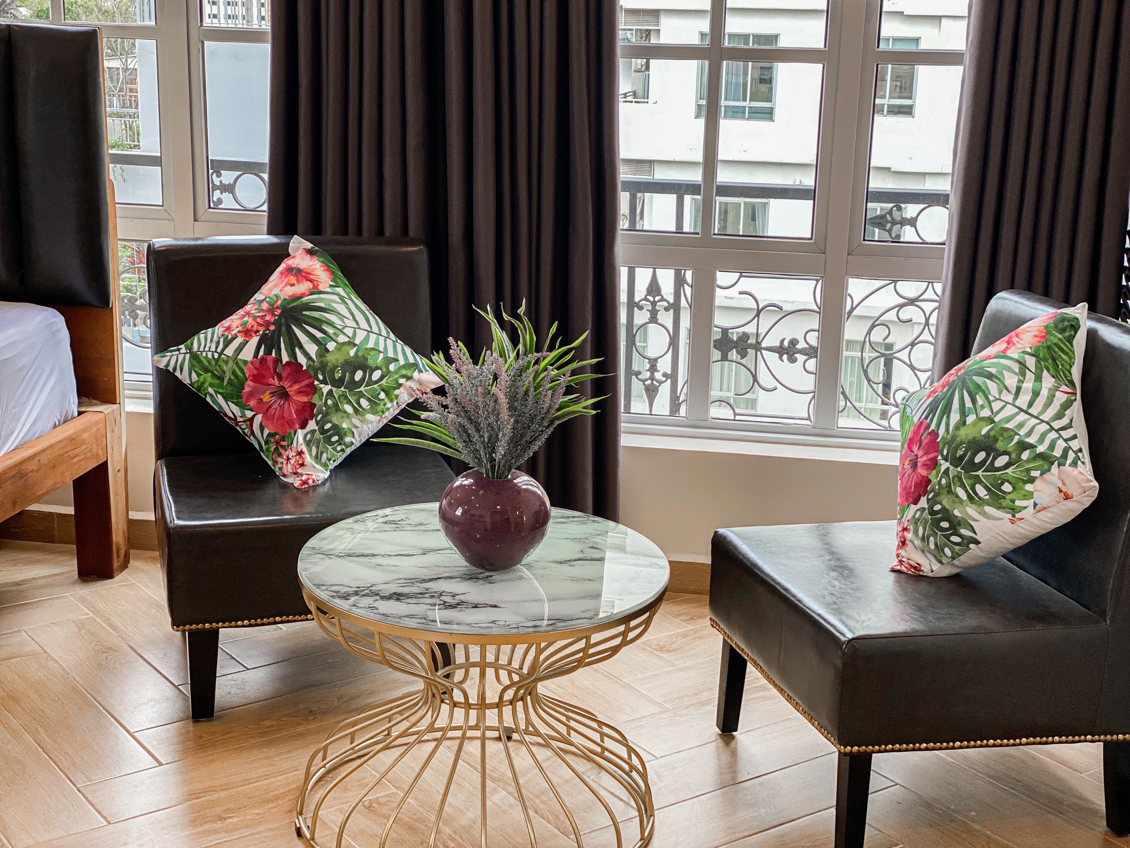 A room with two leather armchairs, a small marble table with a vase, and a view of buildings through large windows.