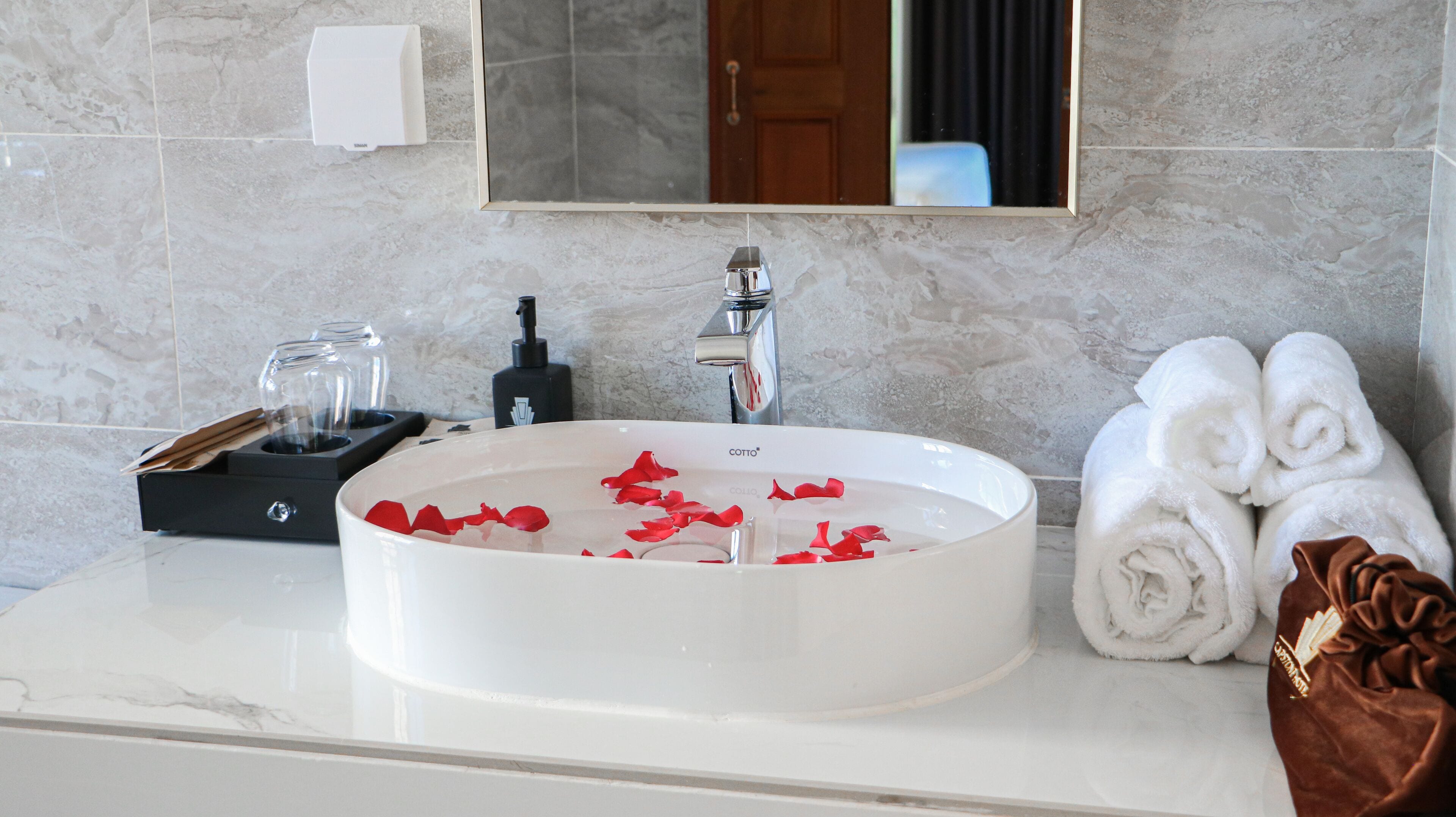A bathroom with a white sink, a mirror, a towel rack with towels, and a soap dispenser.