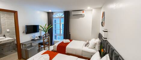 A hotel room with two beds, a desk, a TV, and a bathroom.