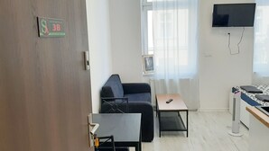 A small, modern room with a sofa, a small table, a TV mounted on the wall, and a bed with a patterned bedspread. - Souvenirappart Sienkiewicza 3B (Bydgoszcz)