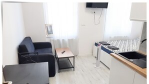 A compact living space with a sofa, a small table, a kitchen area with a sink, and a TV mounted on the wall. - Souvenirappart Sienkiewicza 3B (Bydgoszcz)