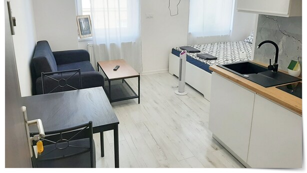 A compact living space with a kitchenette, a sofa, a small table, and a TV mounted on the wall. - Souvenirappart Sienkiewicza 3B (Bydgoszcz)