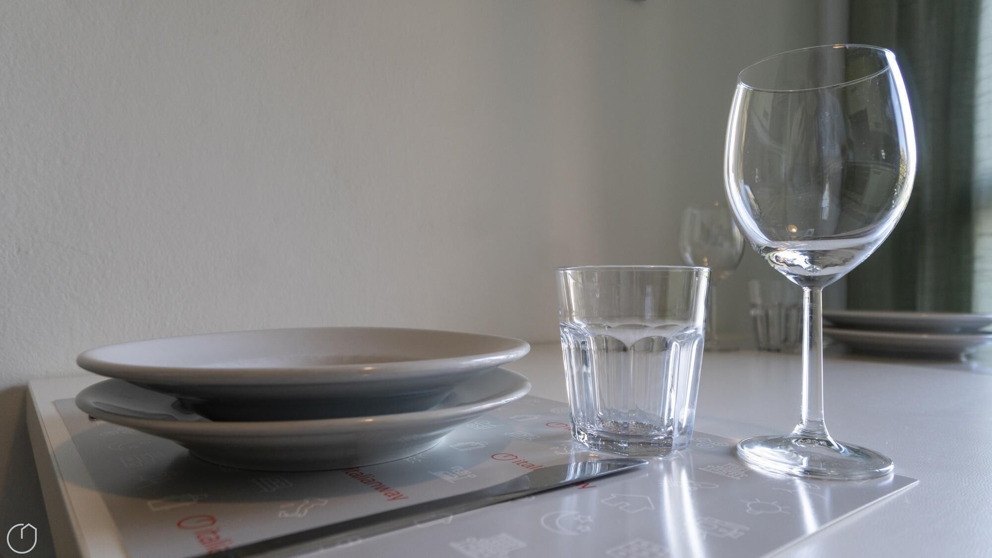 A table with a white plate, a glass of water, and a wine glass.