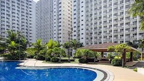 A swimming pool surrounded by palm trees and a high-rise building in the background. - Homefort at Shore 1 Residences (Pasay)