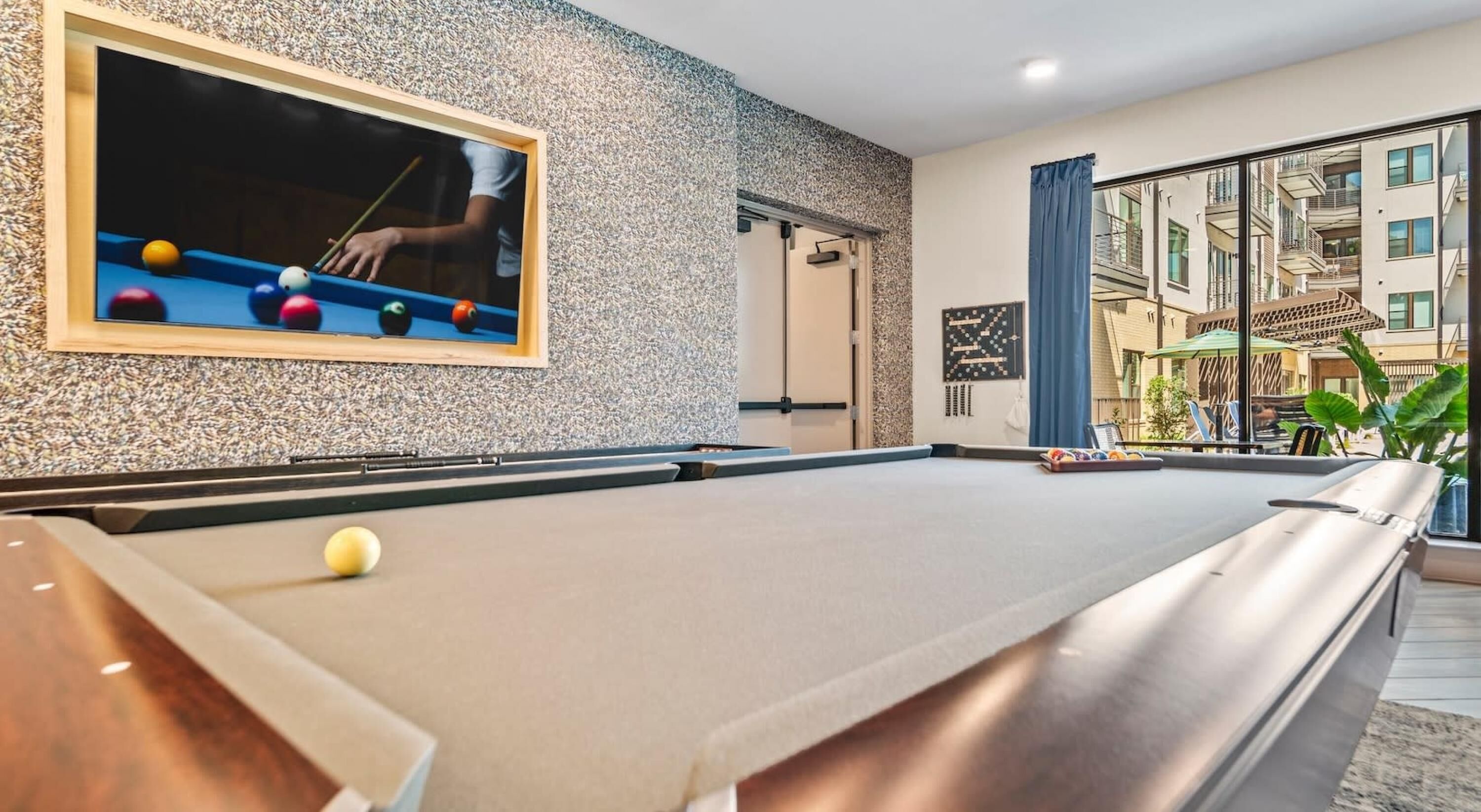 Ein Billardtisch mit Kugeln, ein an der Wand befestigter Fernseher und Blick auf den Balkon.