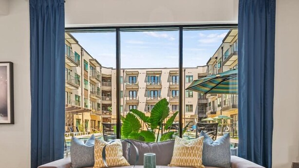 Uma sala de estar moderna com uma janela grande, um sofá, uma mesa de centro e vista para um edifício residencial.