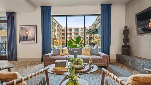 A modern living room with a large window, a sofa, a coffee table with decorative items, and a fireplace. - Chic West Downtown Studio w Washer Dryer (Austin)