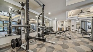 A modern gym with various weightlifting equipment, including a squat rack and dumbbells. - Chic West Downtown Studio w Washer Dryer (Austin)