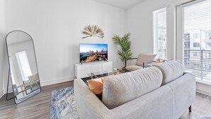 A modern living room with a grey sofa, a flat-screen TV, a large mirror, and a potted plant. - Chic West Downtown Studio w Washer Dryer (Austin)